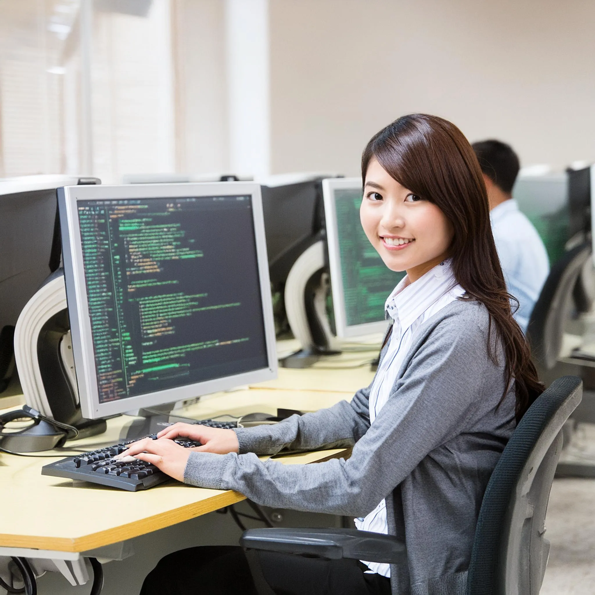 パソコンの前でプログラミングをしている大学生。女性。教室