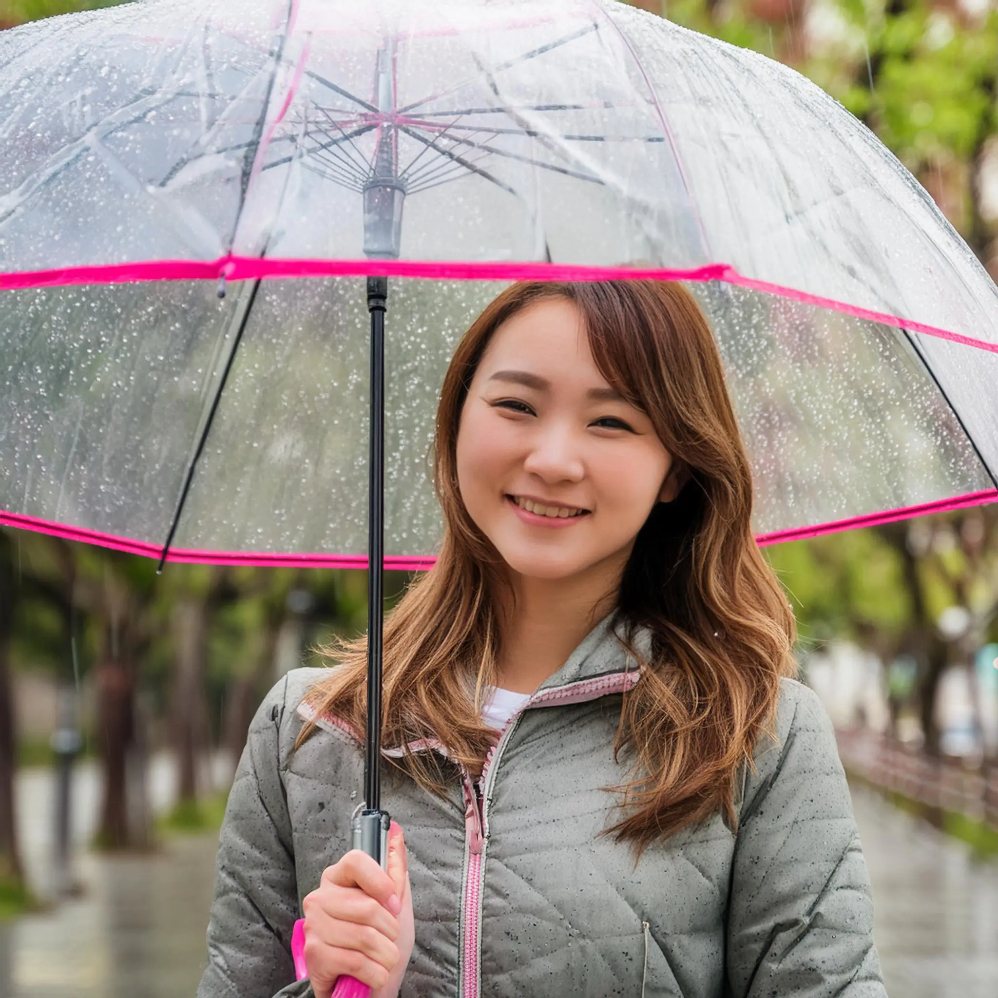 ビニール傘をさしている女性。土砂降り雨。真正面。笑顔。